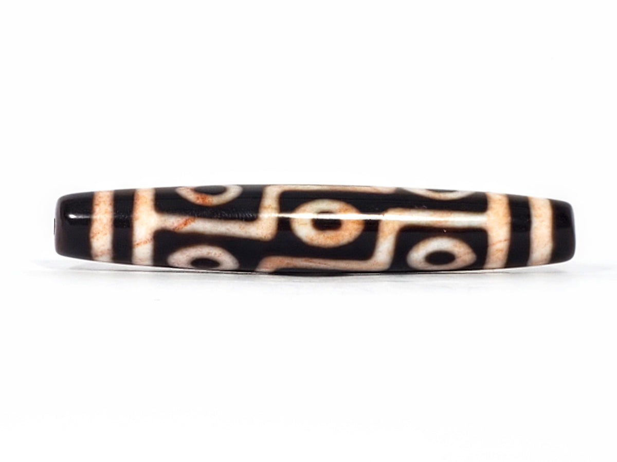 Antique Tibetan nine-eye dzi bead, black agate, white eye motifs, visible bloodspots, natural patina, elongated barrel shape