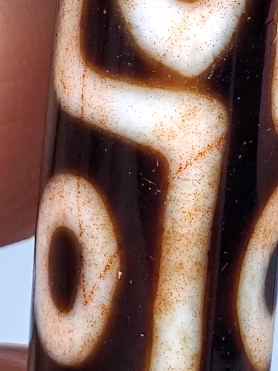 Antique Tibetan nine-eye dzi bead closeup showing cream agate, dark brown etched pattern, orange bloodspots, aged patina