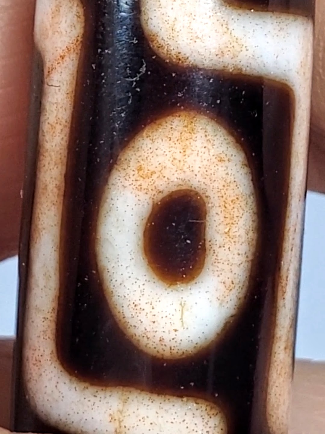 Antique Tibetan dzi bead close-up showing eye motif, cream agate, dark brown patina, bloodspots, aged surface texture