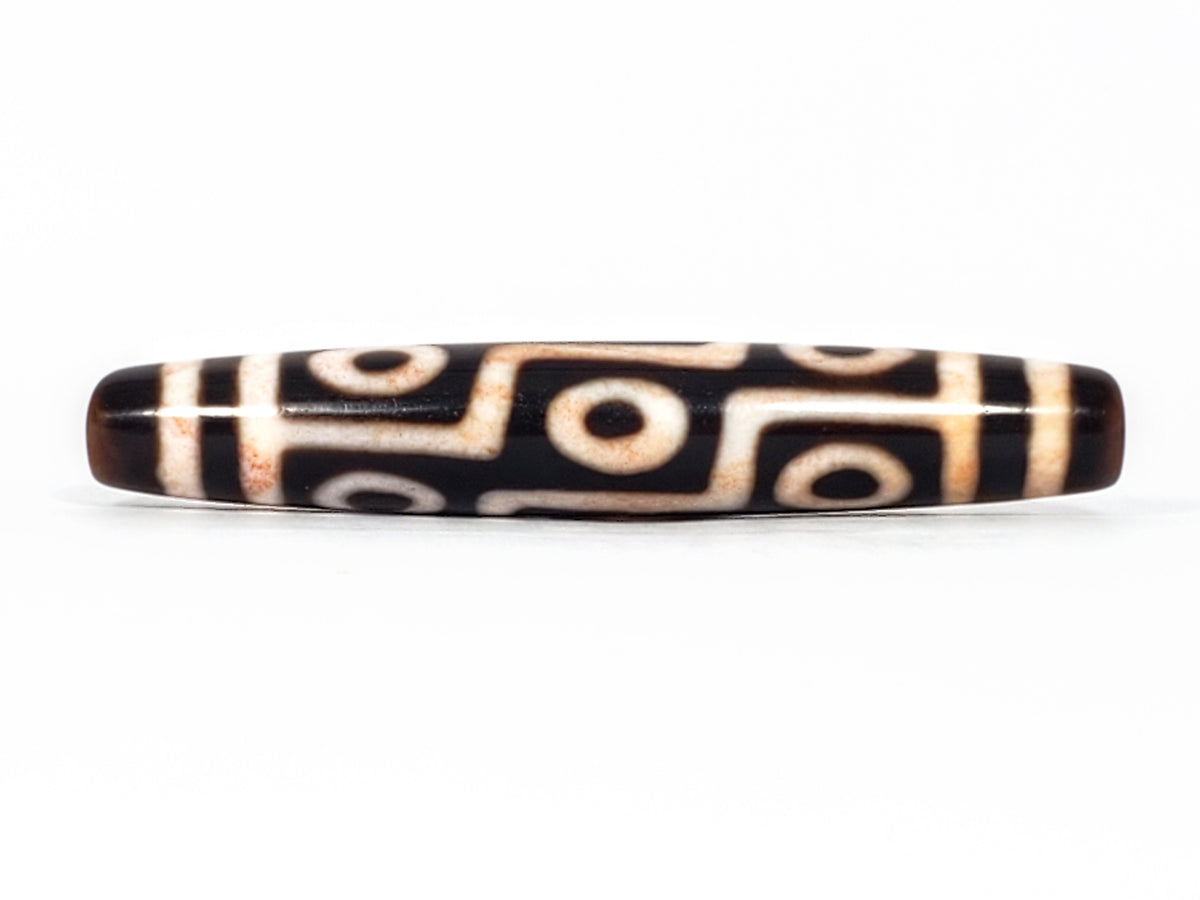 Antique Tibetan nine-eye dzi bead, dark agate, cream eye motifs, visible cinnabar bloodspots, elongated barrel shape
