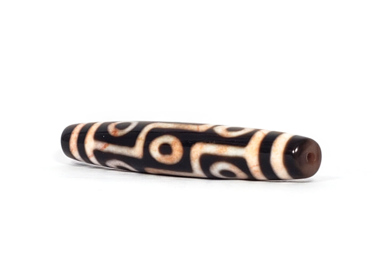 Antique Tibetan nine-eye dzi bead, black agate, white eye motifs, visible bloodspots, patina, drilled ends, elongated barrel shape