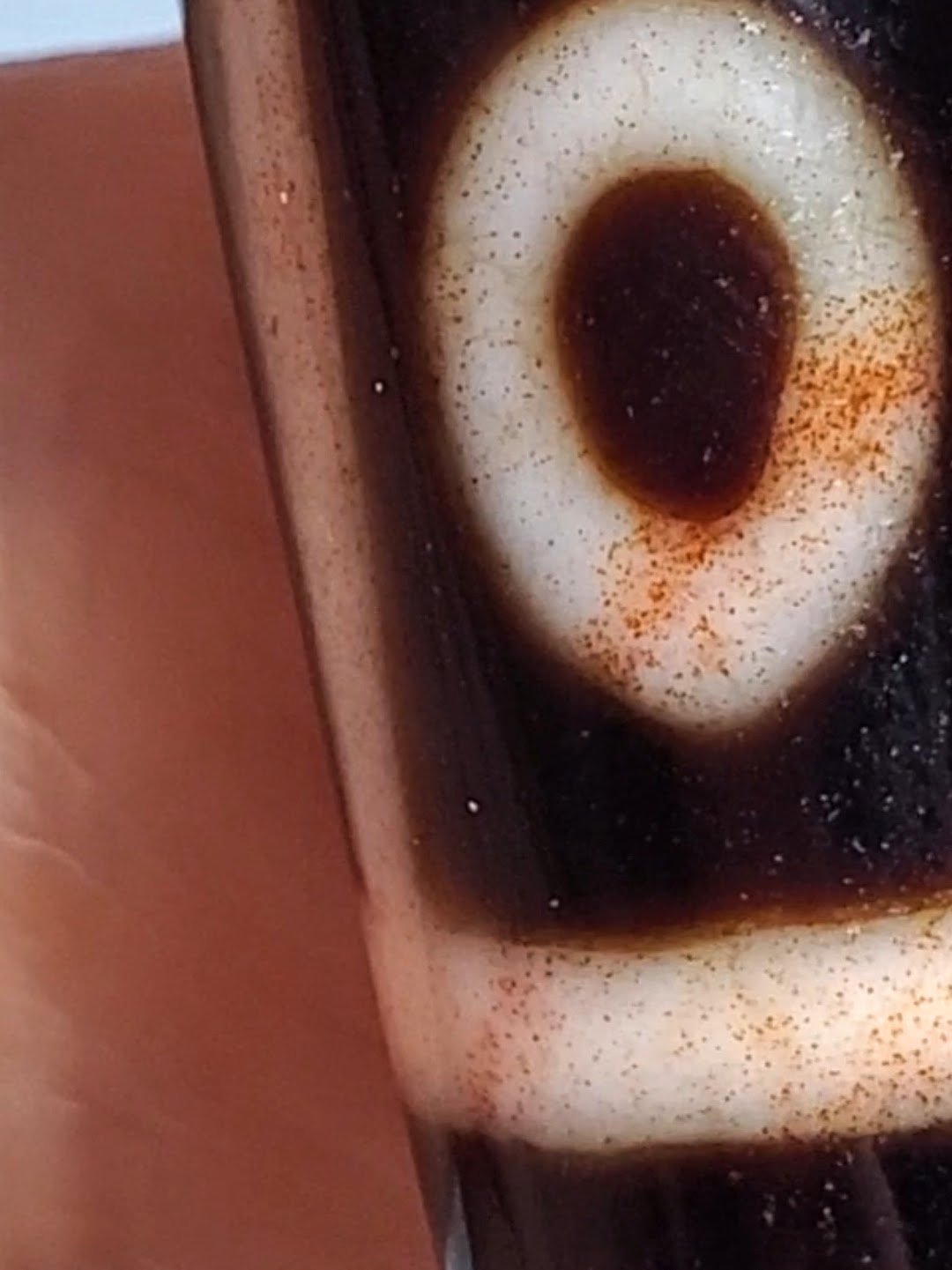 Antique Tibetan dzi bead close-up showing eye motif, white agate, dark patina, orange bloodspots, aged surface texture
