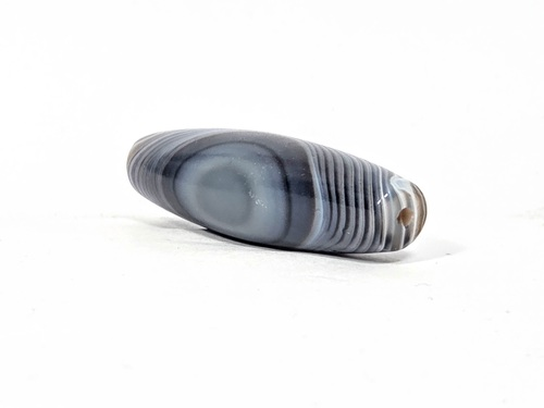 Antique one-eye Dzi bead, grey-blue banded agate, elongated barrel shape, natural patina, visible drill hole, wave striping pattern