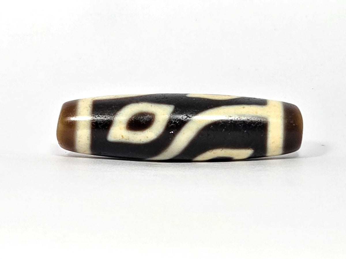 Four-eye dzi bead, dark brown and black agate, cream white eye motifs, wave pattern, polished surface, 40mm elongated barrel shape