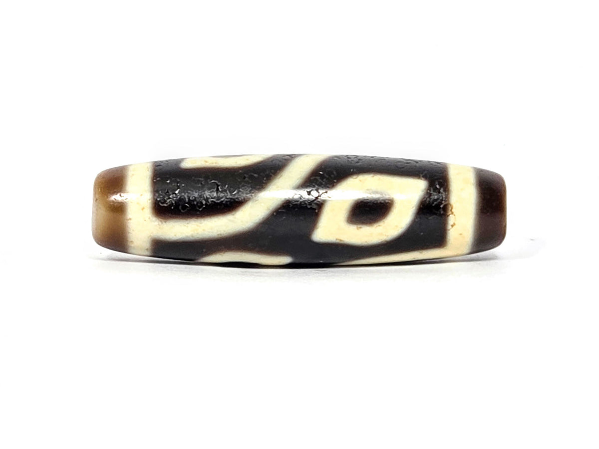 Four-eye dzi bead, dark brown and black agate, cream white eye motifs, elongated oval shape, smooth patina, visible drill hole ends