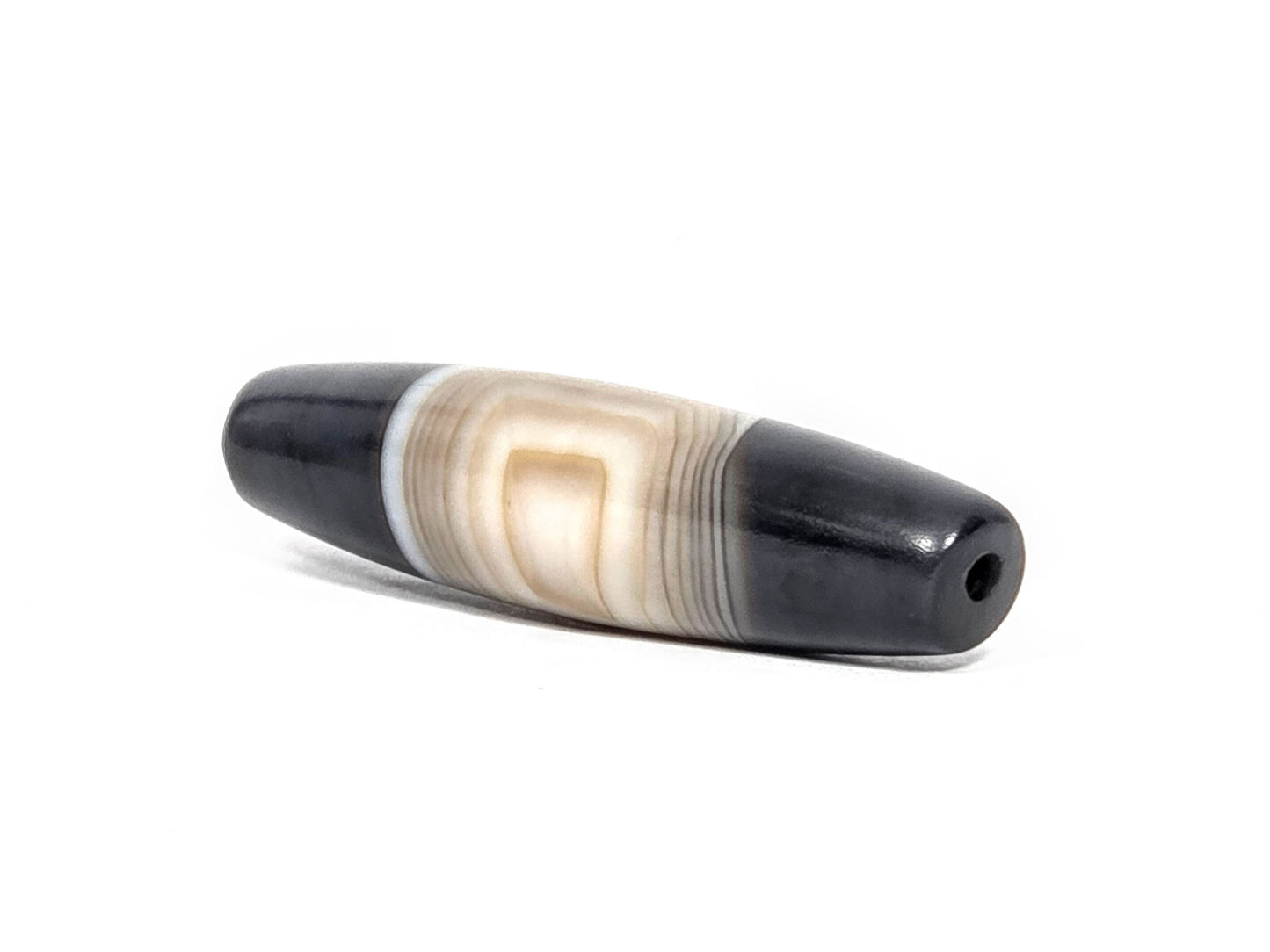 N-N-080426-1E5 natural one eye dzi bead 54.4×14.1mm, angled end view showing warm beige eye composition and pitch-black drill tip, unretouched