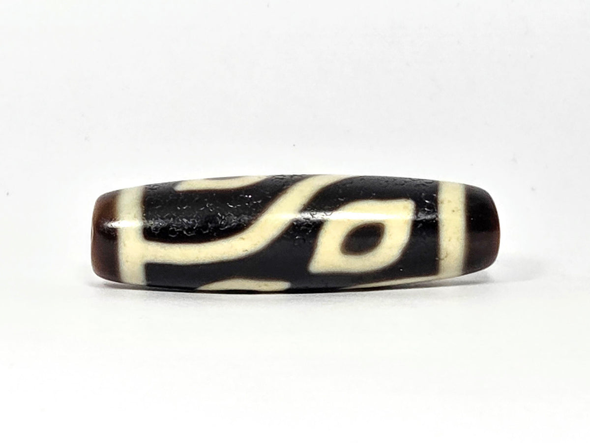 Four-eye dzi bead, dark brown and black agate, white geometric eye motifs, elongated barrel shape, aged patina, 40mm
