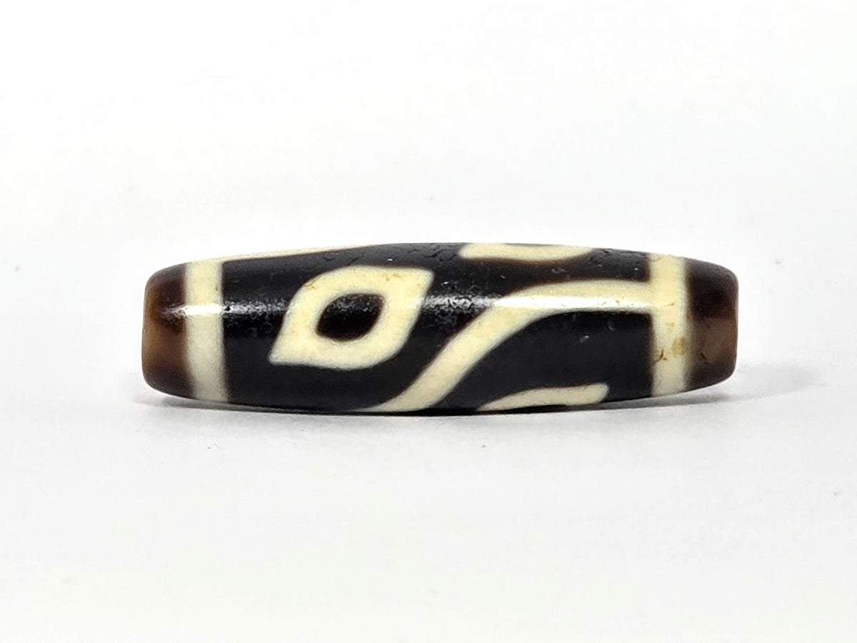 Four-eye dzi bead, dark brown and black agate, cream white eye motifs, wave pattern, aged patina, 40mm barrel shape