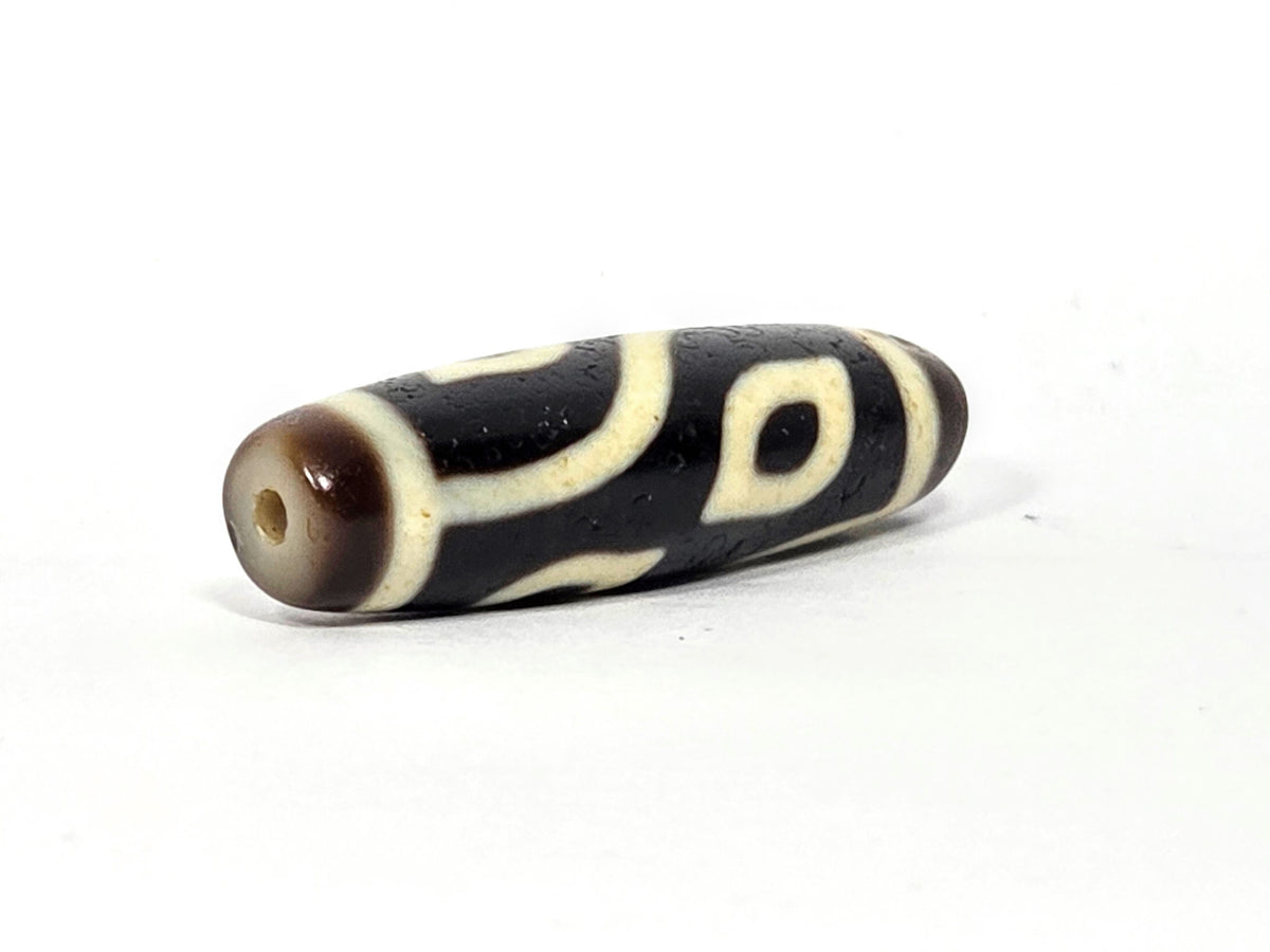 Four-eye dzi bead, dark brown and black agate, cream white eye motifs, visible drill hole, aged patina, 40mm elongated barrel shape