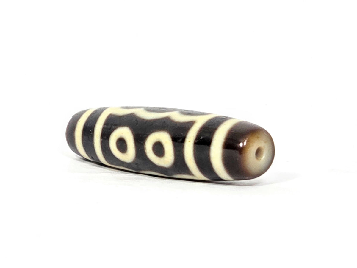 Five-eye dzi bead, dark brown agate, cream eye motifs, stripe bands, visible drill hole, polished surface, 40.5×11.4mm
