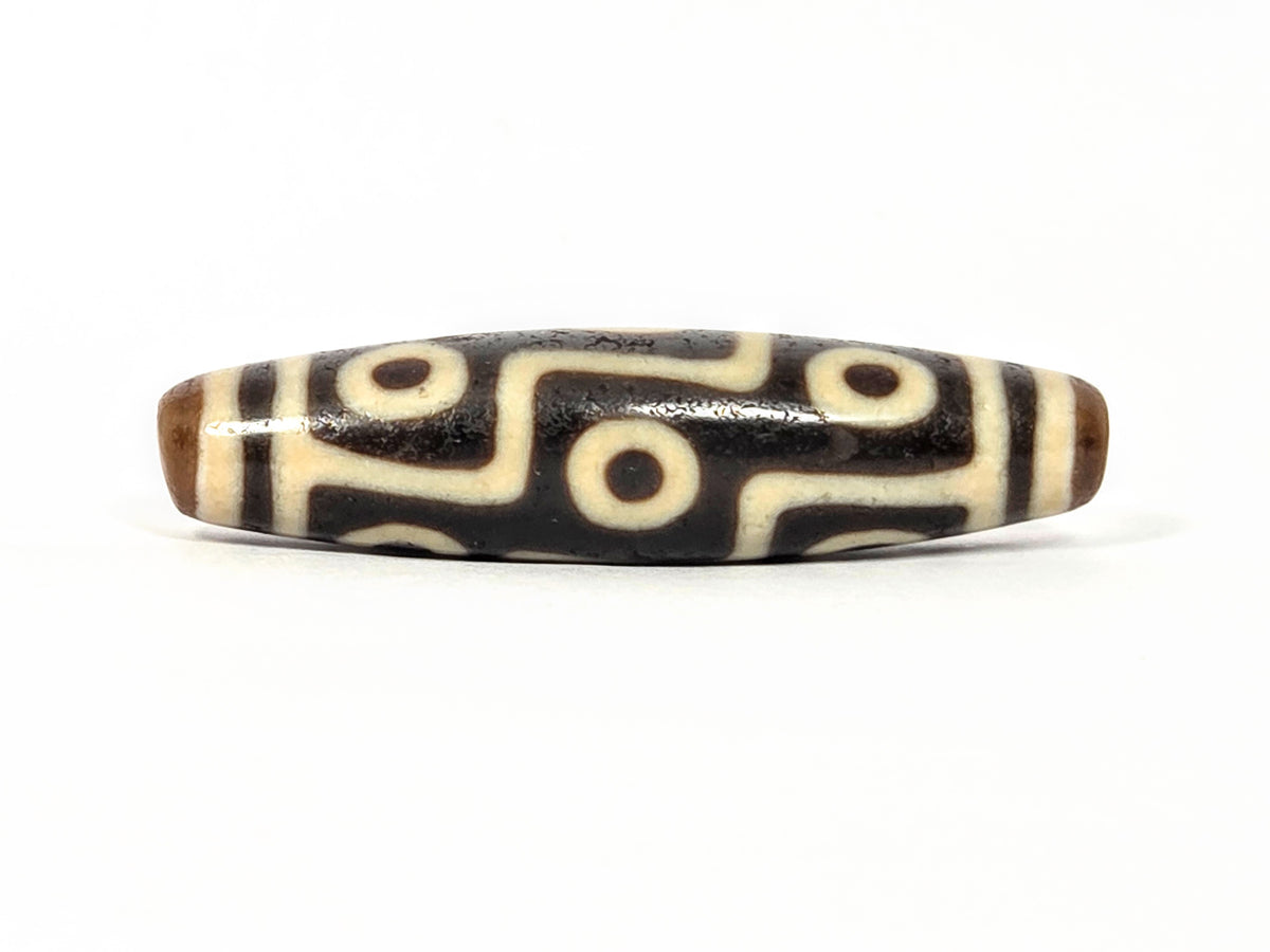Nine-eye Tibetan dzi bead with cream and dark agate stripes, circular motifs, and natural patina