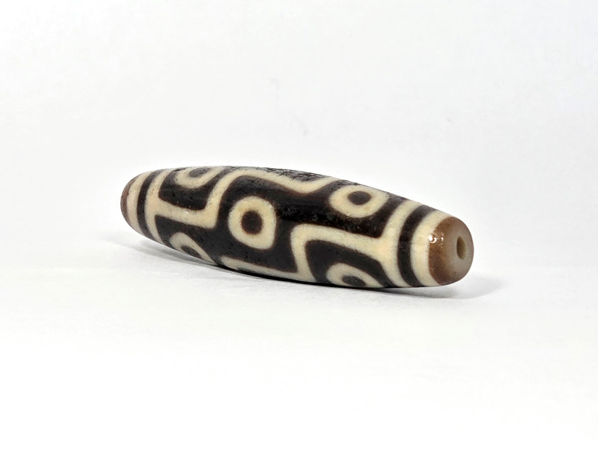 Ancient Tibetan nine-eye dzi bead with cream and black agate patterns, natural drill holes, aged patina surface.
