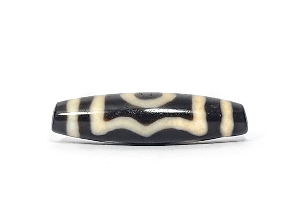 Ancient Tibetan 3-eye dzi bead, black agate, white wave and eye motifs, worn patina, elongated barrel shape