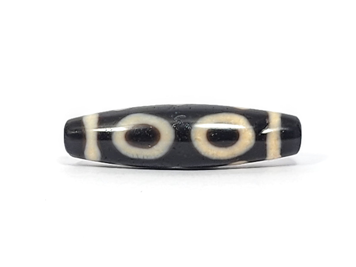 Ancient Tibetan two-eye dzi bead, black agate with cream white eye motifs and stripe pattern, visible drill holes, aged patina