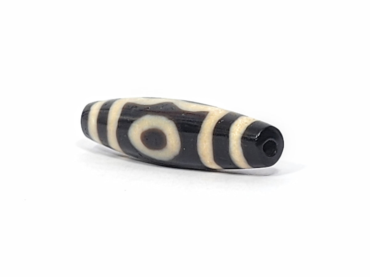 Ancient Tibetan three-eye dzi bead, dark brown agate, cream eye motifs, striped patterning, visible drill hole, aged patina