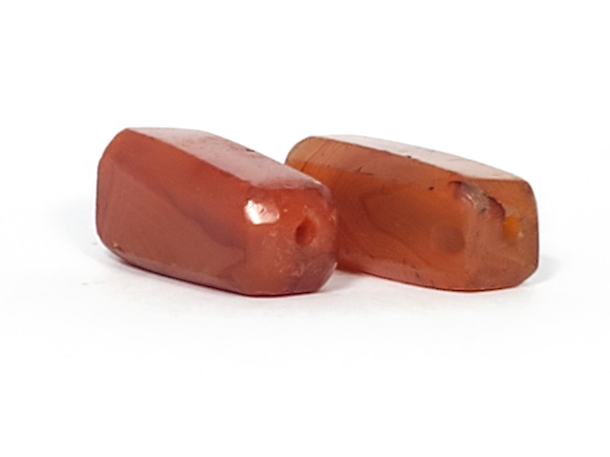 Pair of ancient faceted carnelian beads with reddish-orange hue and visible drill holes