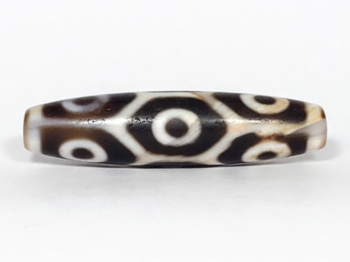 Antique nine-eye dzi bead, dark brown agate with white eye motifs, lotus pattern, aged patina, elongated barrel shape