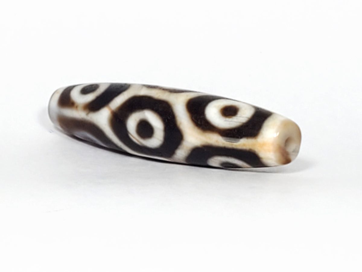 Antique nine-eye dzi bead, elongated agate, dark brown and cream eye motifs, natural patina, visible drill hole at tip