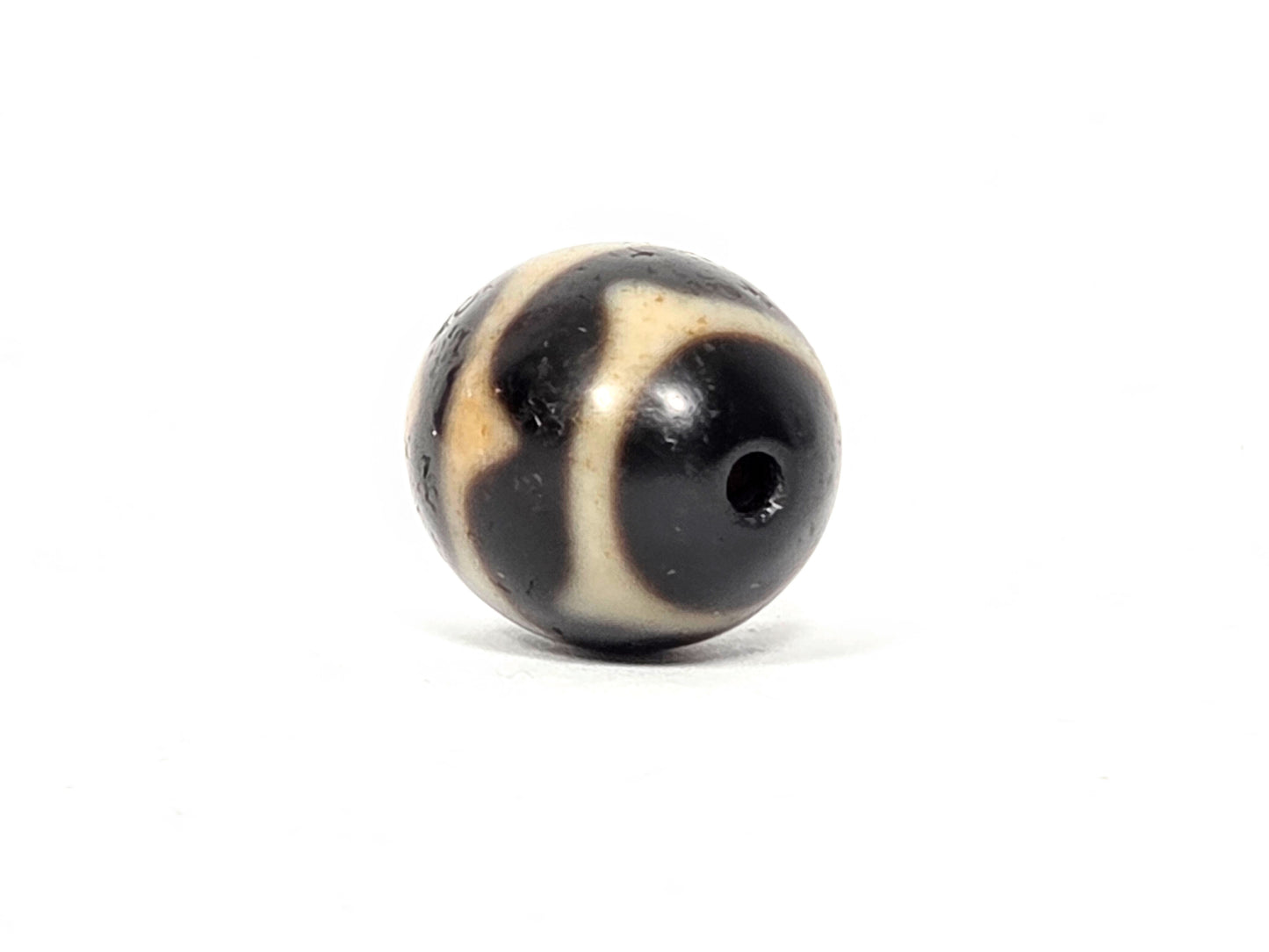 Angled view of single vintage round Double Wave Dzi bead showing depth of wave pattern etching — Taiwan 1980s collectible — unretouched photo — Ancient Dzi Shop