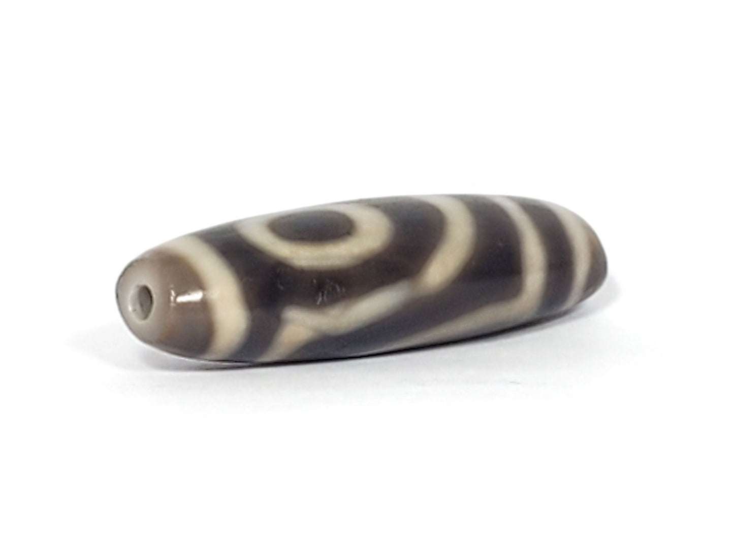 Angled end of ancient Two Eye Dzi — drill hole visible, cream eye wrap-around, slim taper