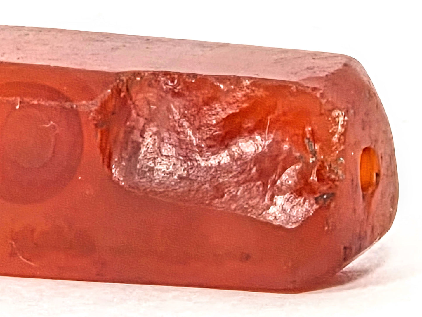 Anc-0626-CBev2, extreme close-up of ancient chipping and intact drill hole at end face, translucent carnelian, unretouched