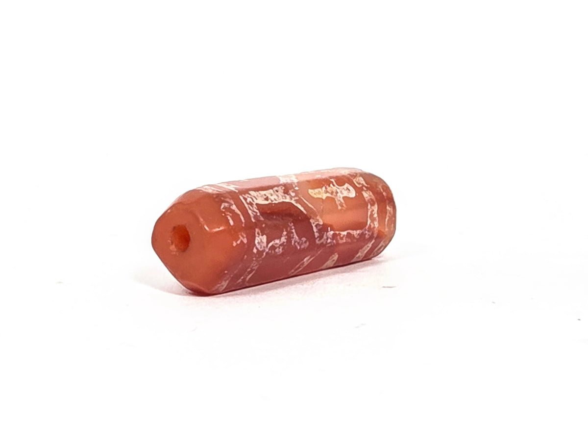 Opposite angled end view of ancient etched carnelian cross and longevity bead (AC-101026-CL6) showing tapered narrower end with drill hole and warm brick-red carnelian end face, octagonal facets visible