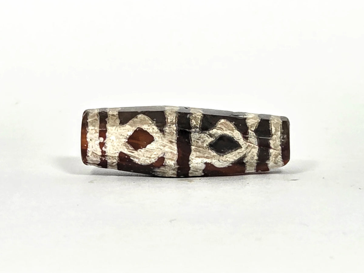 Ancient etched carnelian bead AC-101226-EC, first lateral profile showing eight-sided faceted barrel form with silver-white lime etching and diamond-eye geometric motif on warm reddish-brown carnelian ground, 700–1000 years old