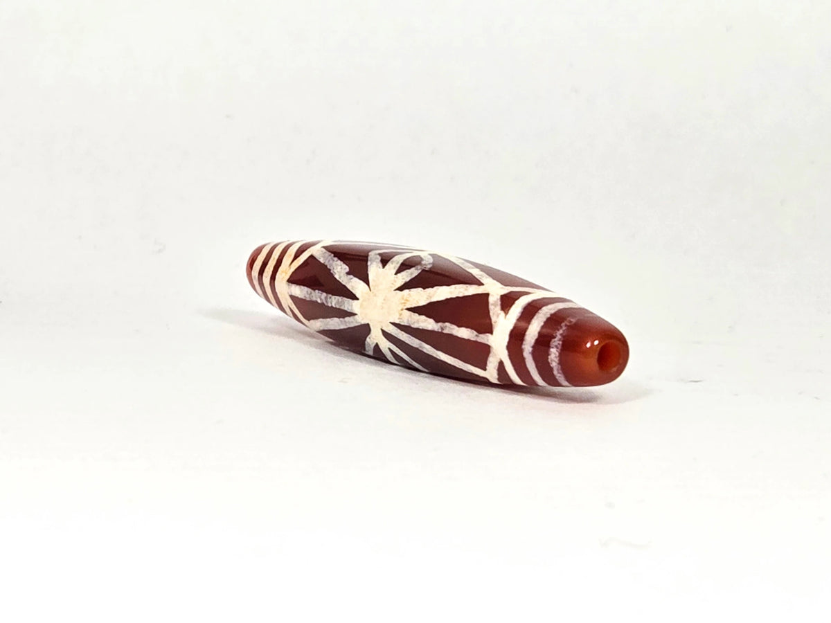 Opposite end view of ancient etched carnelian starburst bead AC-101026-CS showing second drill hole in warm amber carnelian tip and band line transition from body to end cap