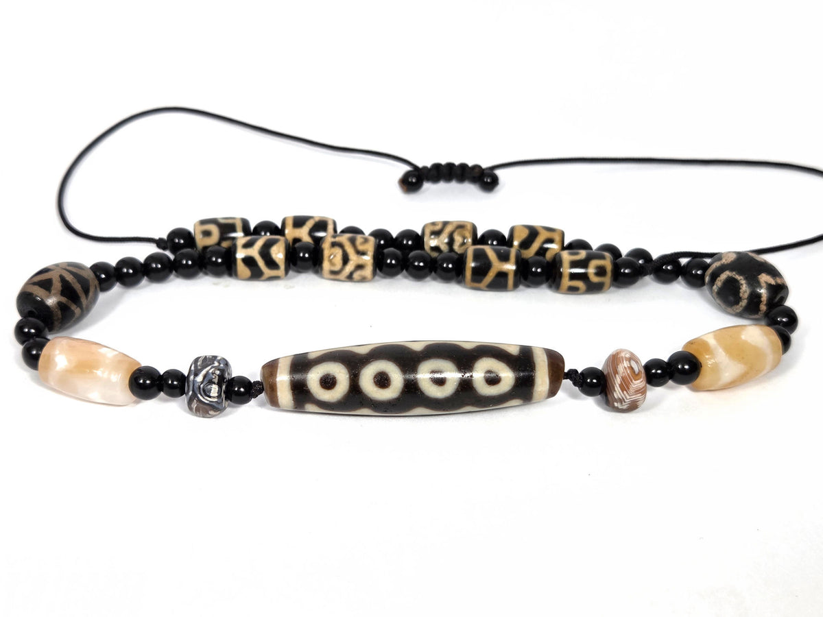Seven-eye dzi bead necklace, dark agate focal bead with white eye motifs, black onyx spacers, carved tube beads, adjustable cord
