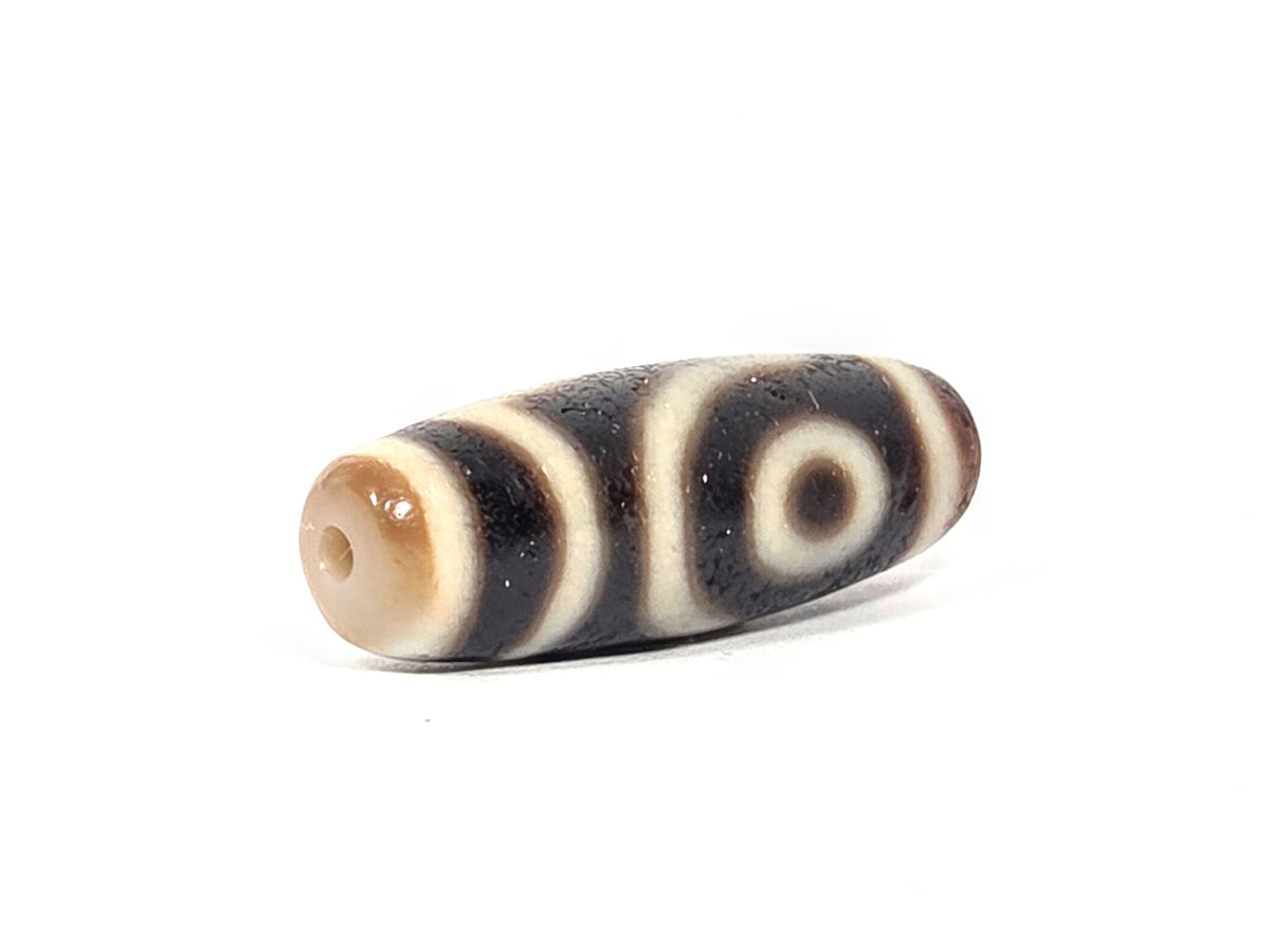 Two-eye dzi bead, pitch-black and cream agate with natural banding, drilled holes, ancient patina