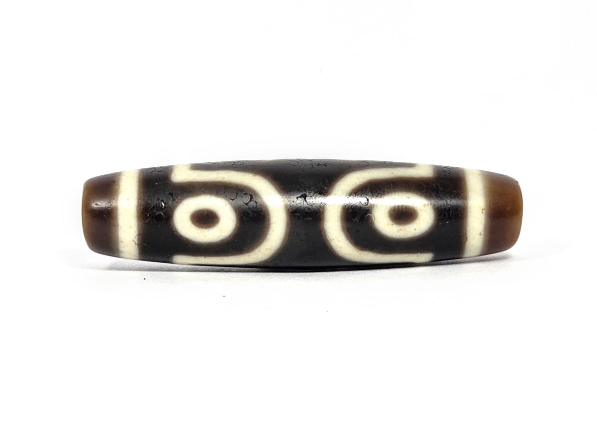 At-072226-7E Seven Eye face C — paired eyes with S-curve wave connectors, bold cream motif lines, unretouched.