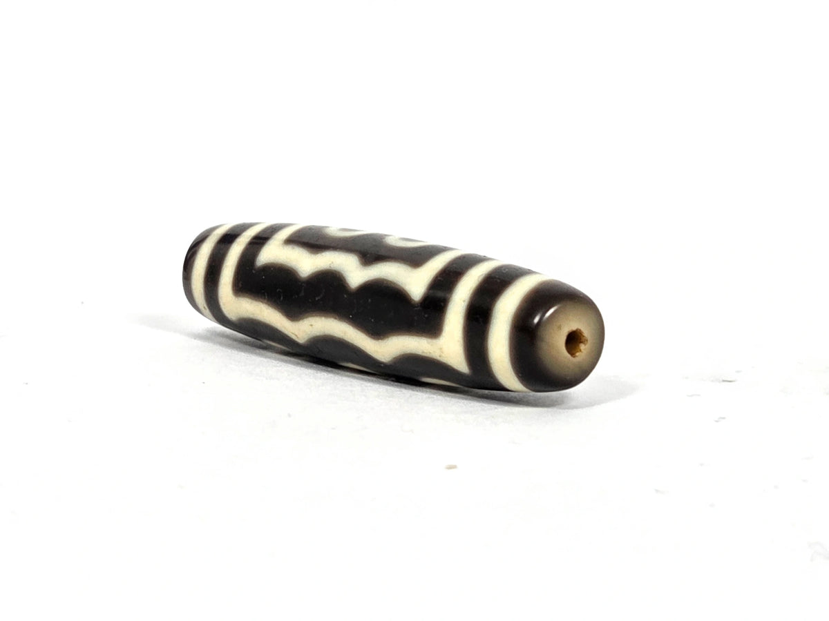 Angled end view of antique Tibetan five-eye dzi bead (AT-100826-5E) showing small clean drill hole in warm grey-brown agate end cap, 200–400 years old