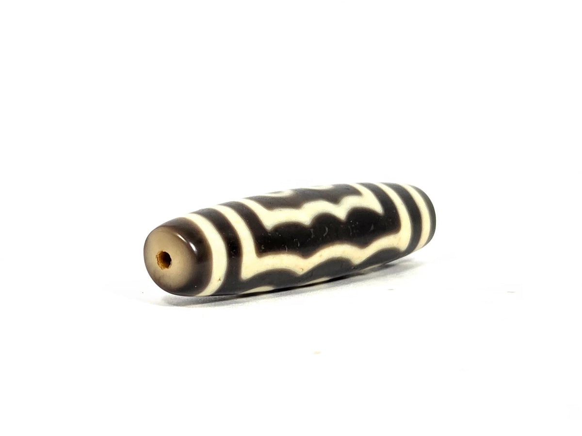 Opposite end view of antique Tibetan five-eye dzi bead showing second drill hole and warm grey-brown agate end cap with wave pattern continuing to the tip