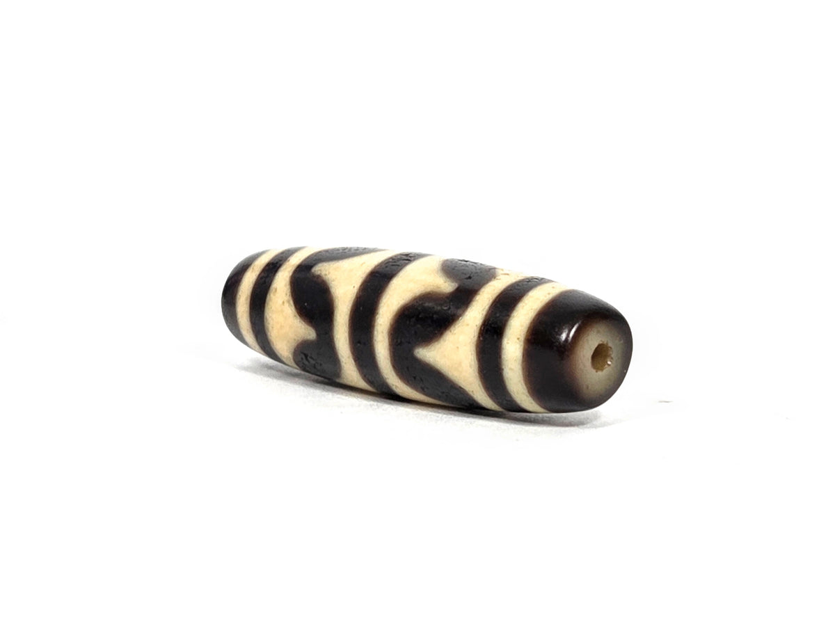 Angled end view of antique Tibetan double wave dzi bead showing small clean drill hole set in warm brown-black agate end cap, 200–400 years old