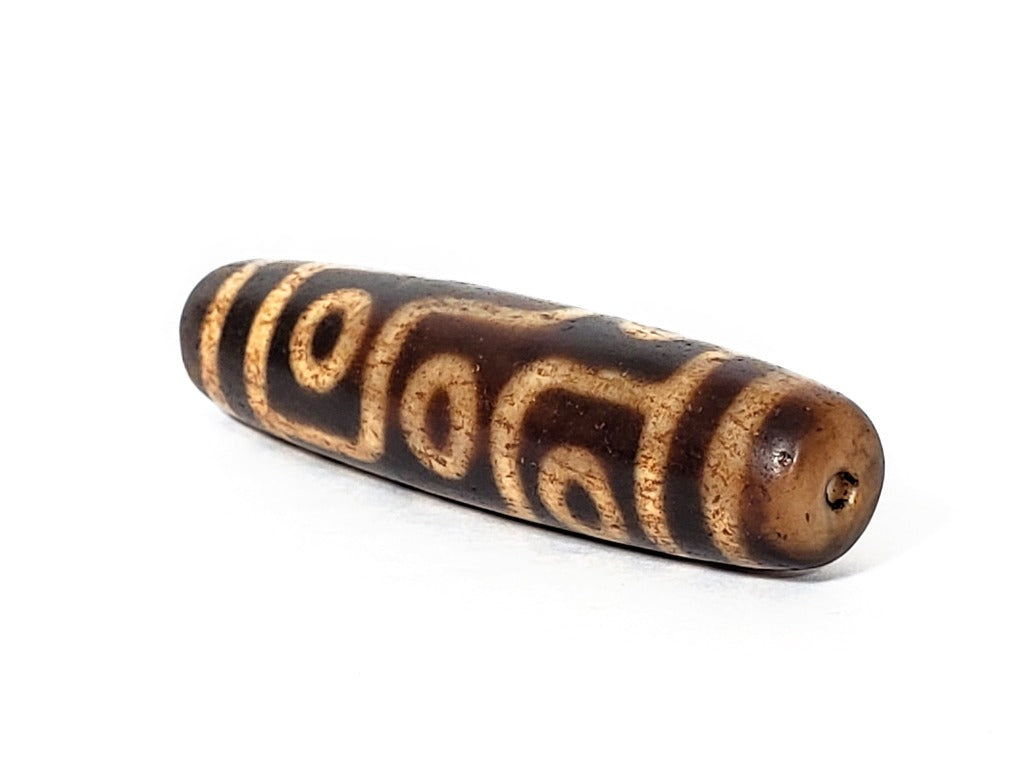 A vintage Dzi bead with a faux antique appearance featuring a mesmerizing nine-eye motif. The intricate carvings and weathered texture give it an ancient look, evoking a sense of spiritual power and wisdom. The nine eyes symbolize protection, insight, and spiritual enlightenment.