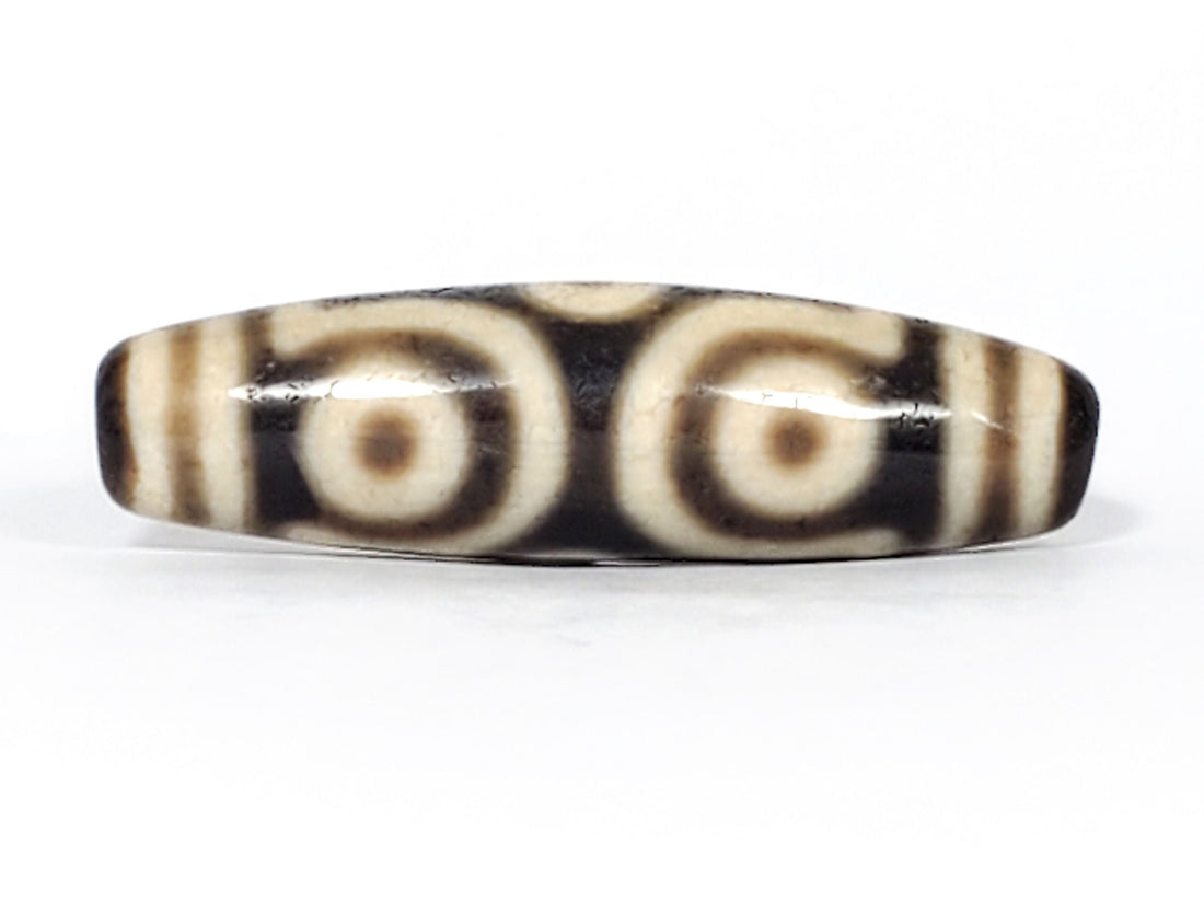 Ancient Tibetan six-eye dzi bead — near-black agate with large bold cream eye motifs and scroll dividers, showing natural surface patina and heavy agate contrast consistent with extreme age, unretouched photo by Ancient Dzi Shop