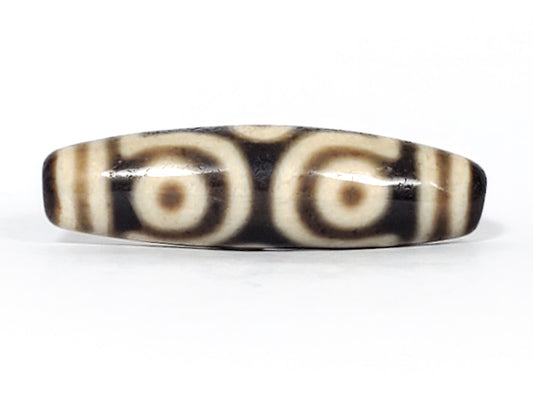 Ancient Tibetan six-eye dzi bead — near-black agate with large bold cream eye motifs and scroll dividers, showing natural surface patina and heavy agate contrast consistent with extreme age, unretouched photo by Ancient Dzi Shop