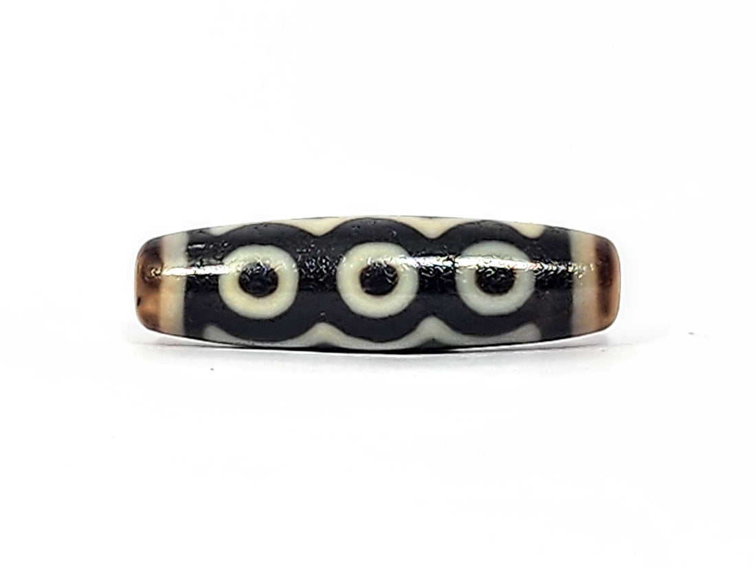 Antique Tibetan five-eye dzi bead, deep dark ground, cream eyes linked by wave band, warm brown end caps, unretouched