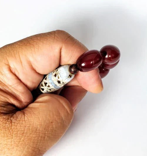 Authentic Tibetan Dzi bead held in hand alongside deep red carnelian mala beads — Ancient Dzi Shop