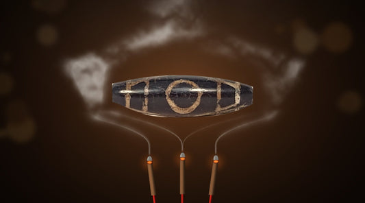 Ancient two eye Tibetan dzi bead held above burning incense sticks as smoke rises around it for a traditional blessing