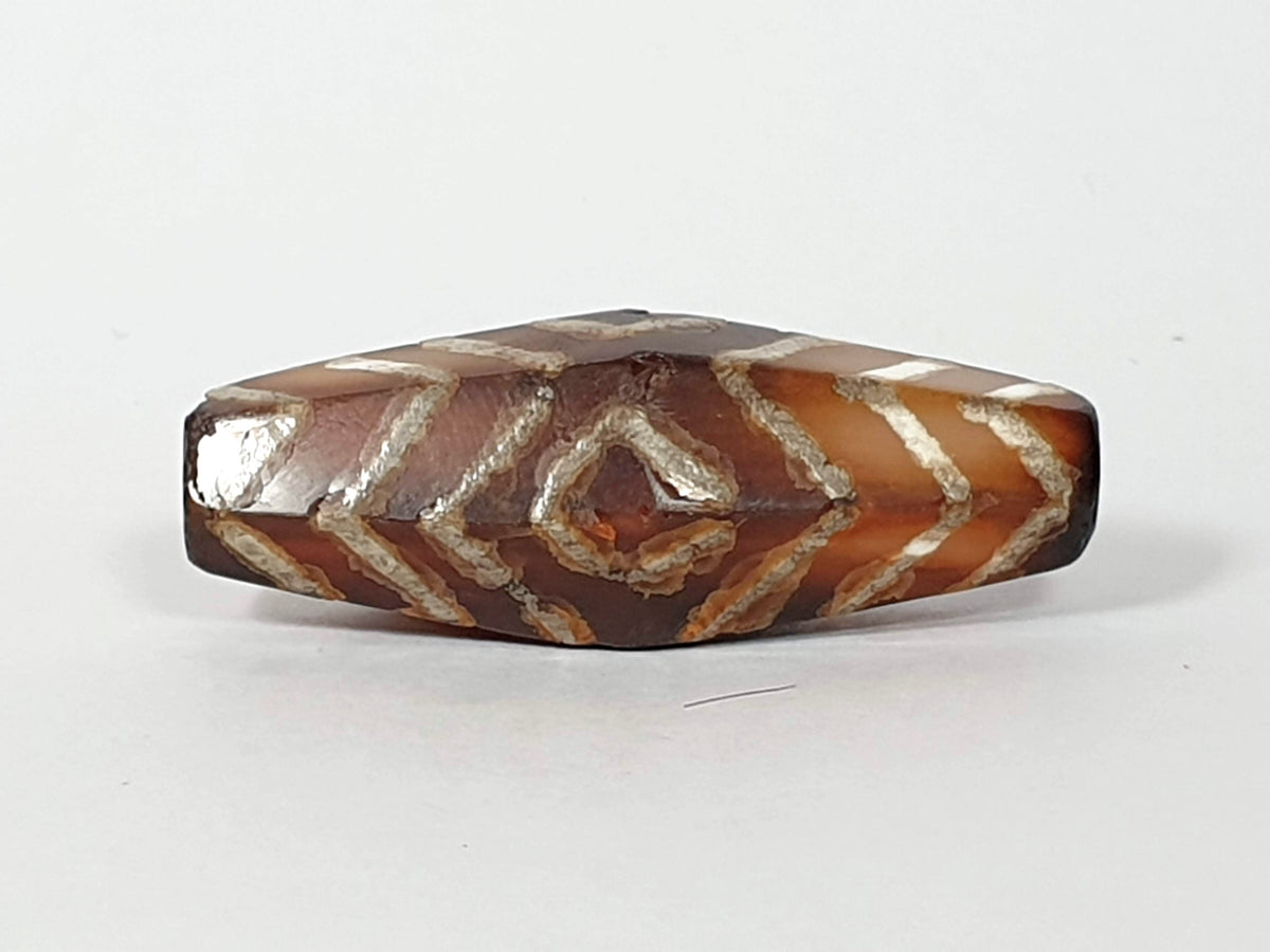 Ancient carnelian dzi bead hexagonal shape three-eye tiger stripe motif etched white lines brown agate patina visible