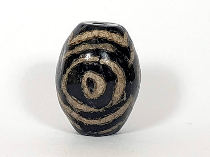 Black agate dzi bead with tan spiral triple heaven's gate motif, visible drill hole, aged patina surface texture