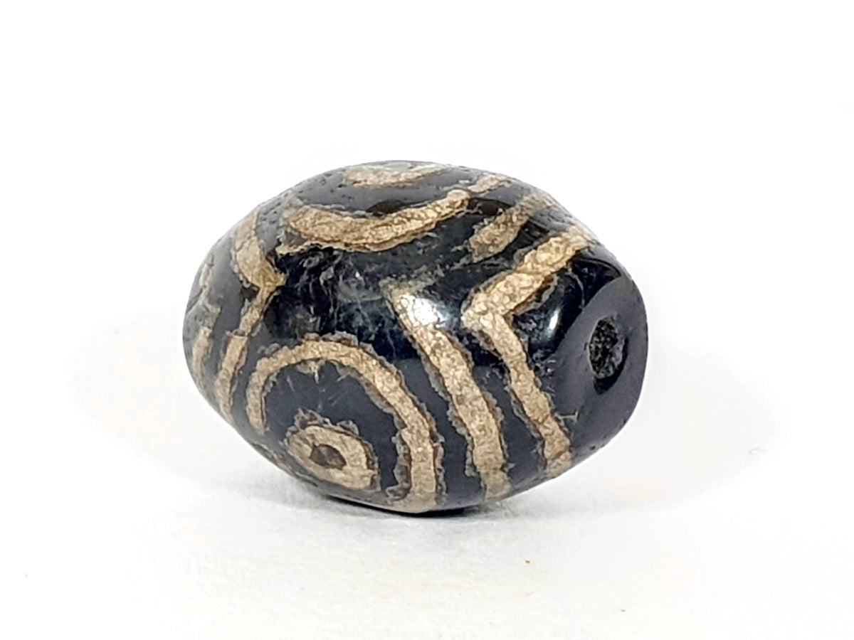 Ancient triple heaven's gate motif dzi bead, black agate, tan etched spiral patterns, visible drill hole, aged patina surface