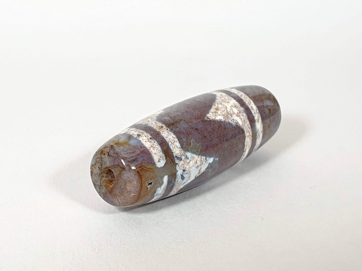 Tiger tooth agate dzi bead with white stripes and bloodspots on brown stone surface
