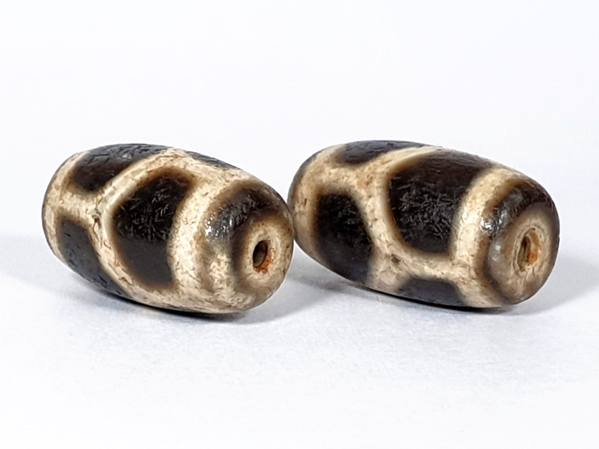 N-FA-062626-LG pair longevity dzi, angled end view, drill holes, rust-orange interiors, cream sandy ground, unretouched