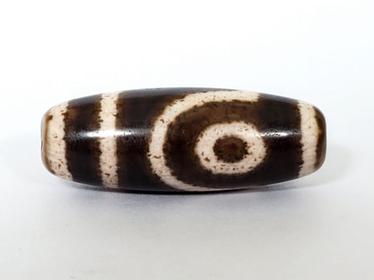 Antique Qing Dynasty two-eye dzi bead, dark brown agate, cream spiral eye motifs, striped patterning, aged patina surface.