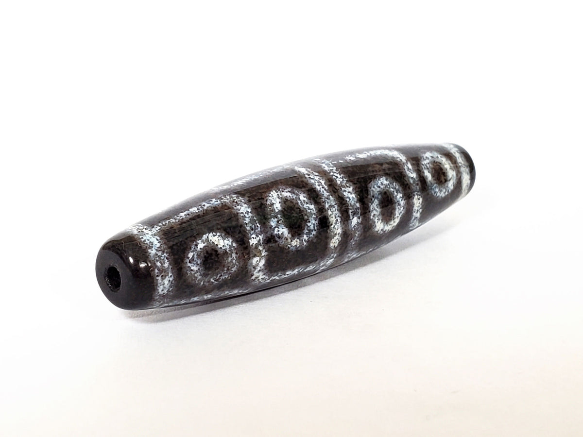 Twelve eye motif dzi bead with white circular patterns and bloodspots on dark agate, center drill hole visible