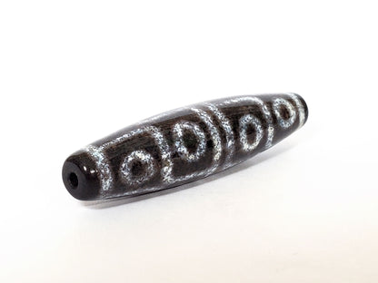 Twelve eye motif dzi bead with white circular patterns and bloodspots on dark agate, center drill hole visible