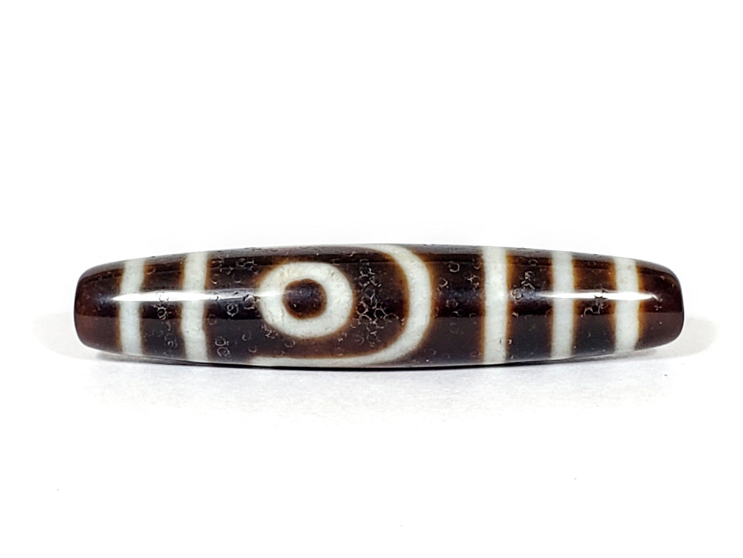 V-070226-2E vintage two eye dzi bead, front view, dark brown ground, cream eye motif, 56.6×11.9mm, unretouched.