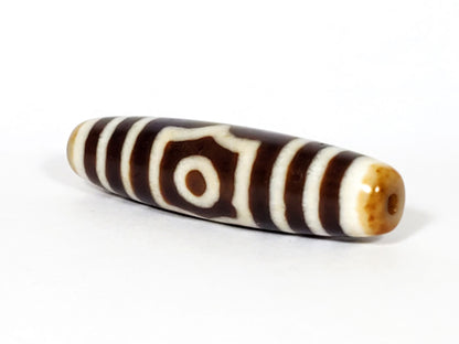 Opposite end cap of antique three eye dzi At-053126-3E, warm honey-tan agate tip with drill hole, single-eye frame face visible, elongated torpedo 51.2mm, unretouched photography